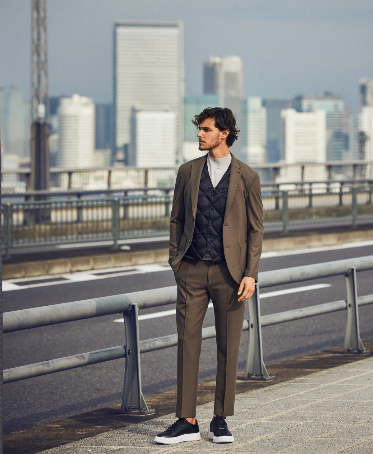 カーキのベスト・グレーのパーカー・チャコールグレーのパンツを履いた外人男性