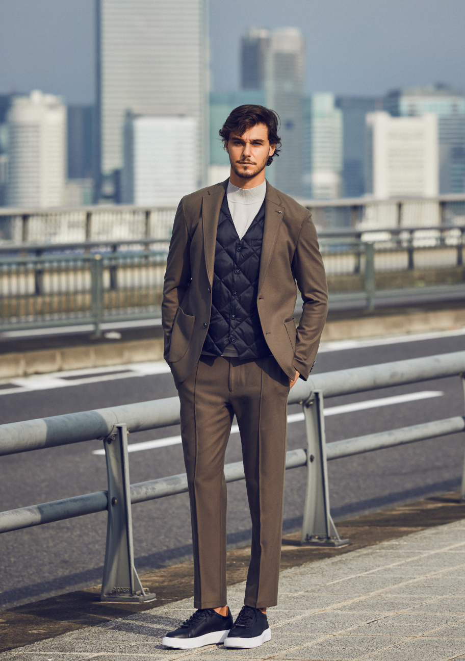 カーキのセットアップ・ブラックのベスト・ライトベージュのニットを着た外人男性