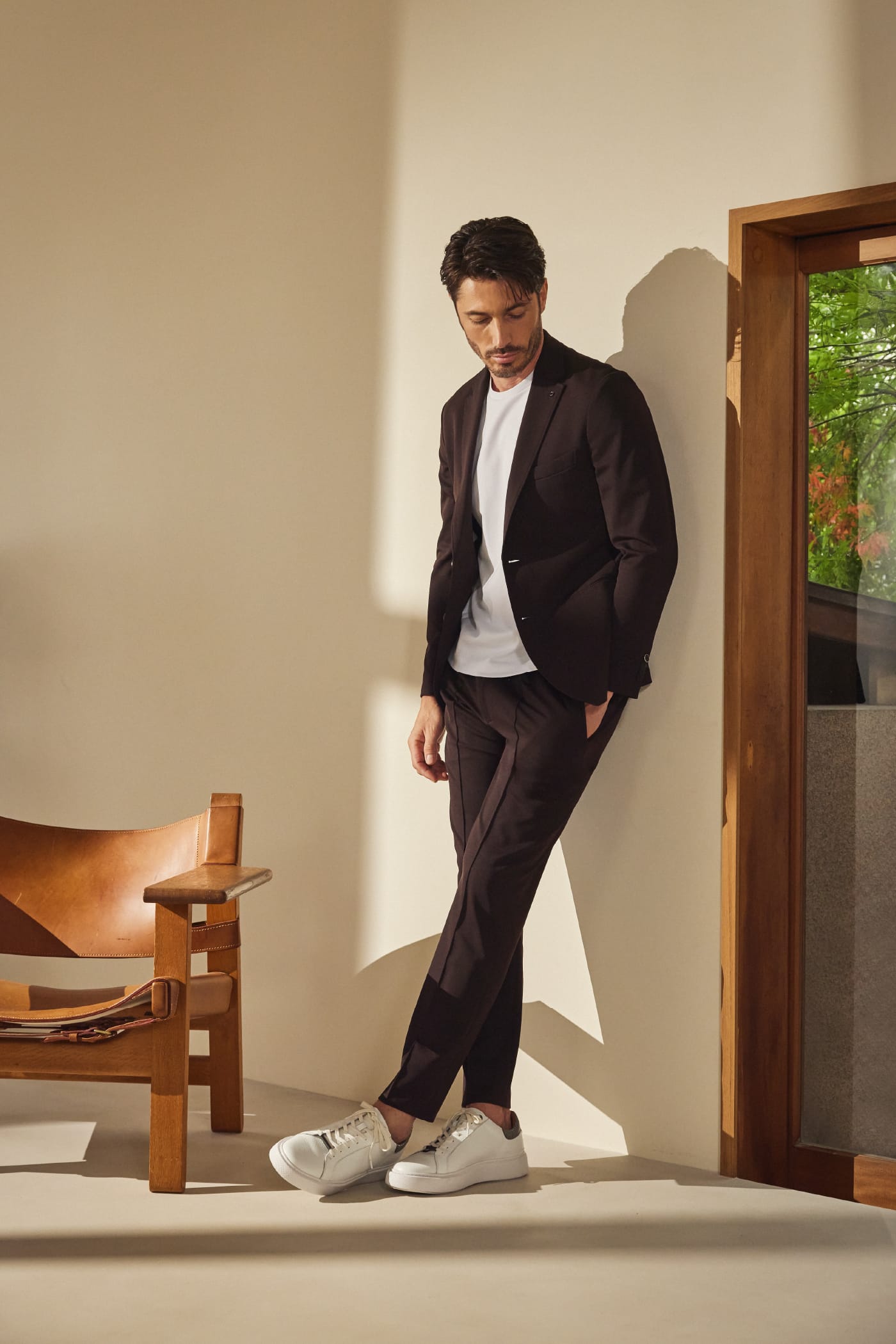【CERIMONIA】ブライトツイルジャージ ジャケット、PABLO ビジネスTシャツ、【CERIMONIA】ブライトツイルジャージ パンツ、【ONLINE限定】DEVICE1 スニーカー パイソンスタンプを着用し、左手をポケットに入れて下を向いている男性モデルの全体画像
