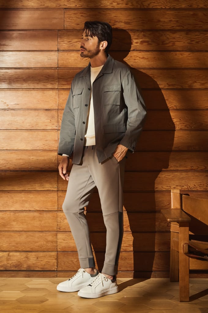 マッドシャイン４パッチシャツアウター、VECCHIO パンツ、【ONLINE限定】DEVICE1 スニーカー パイソンスタンプ、テックスブリッド クルーネックニットを着用して腰に手を当てている男性モデルの全身画像