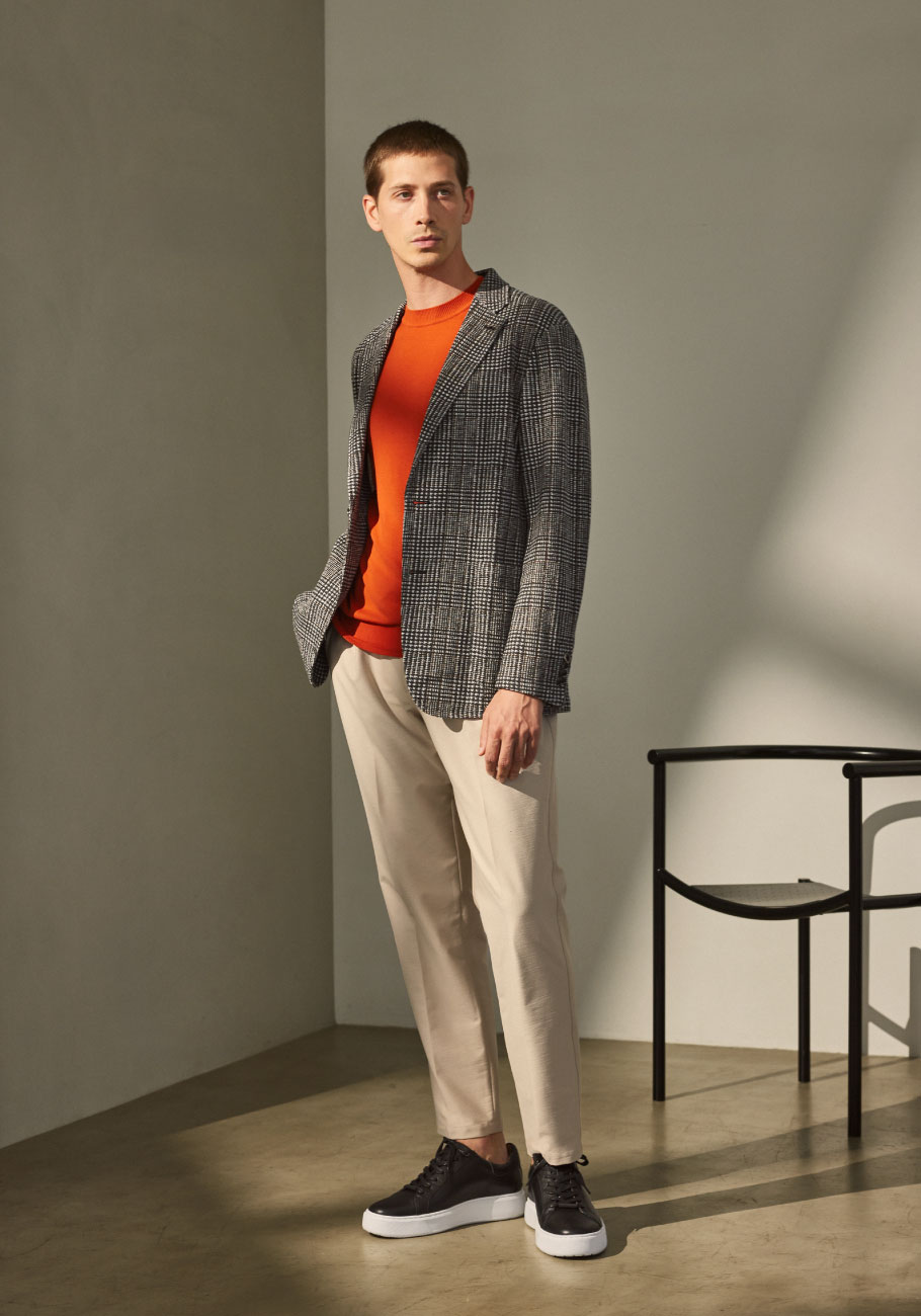 ベージュのパンツ・オレンジのトップス・グレーのチェック柄のジャケットを着用した男性