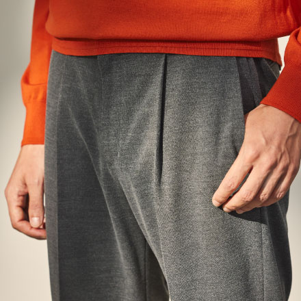 オレンジのニットとグレーのパンツを履いた男性