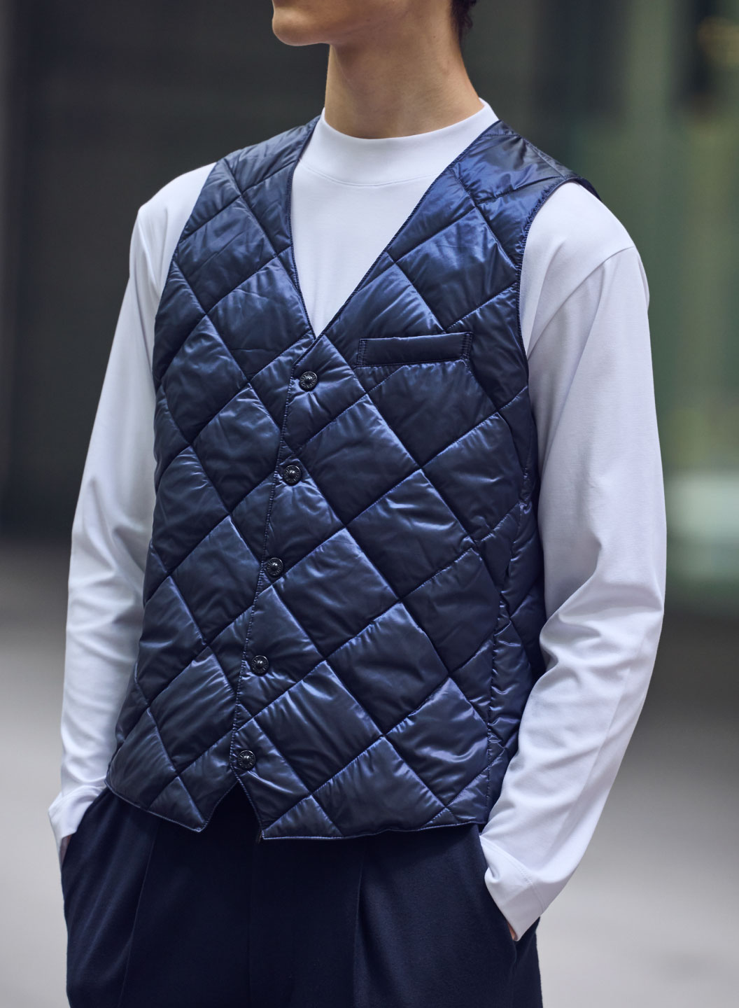 ネイビーのジャケット・ネイビーのジレ・ホワイトのトップス・ネイビーのパンツ・ホワイトのスニーカーを着用した、高身長男性