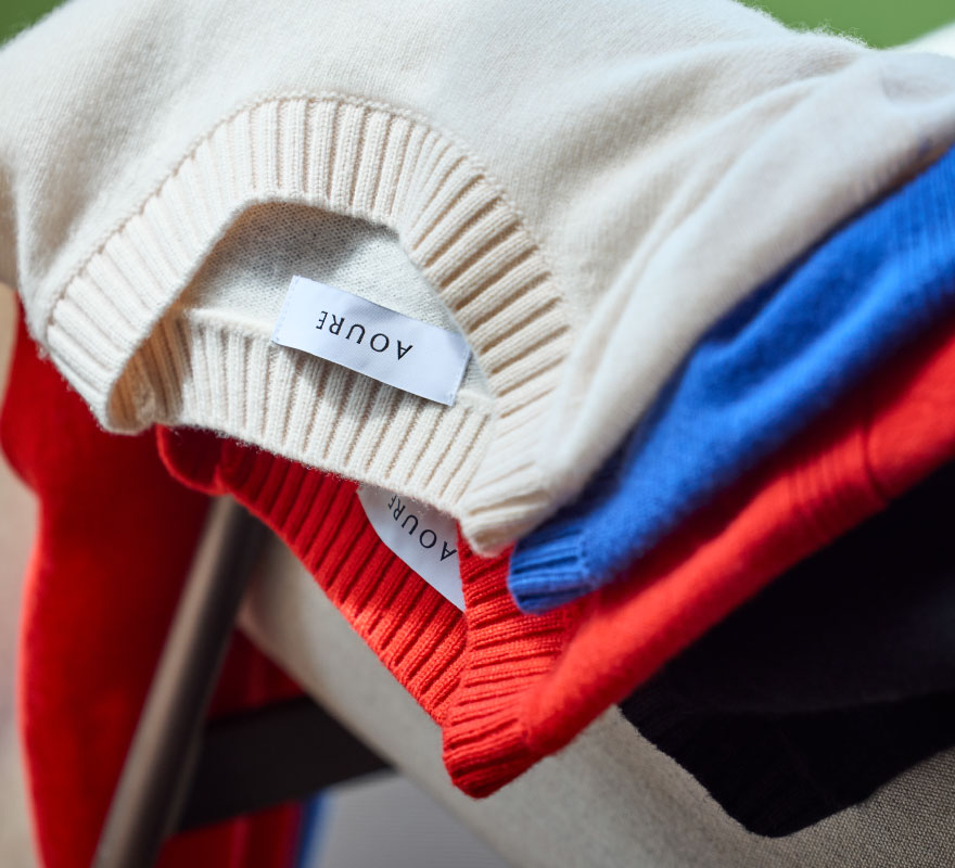 ホワイト・ブルー・レッド・ブラックのニットがソファーに置かれている様子