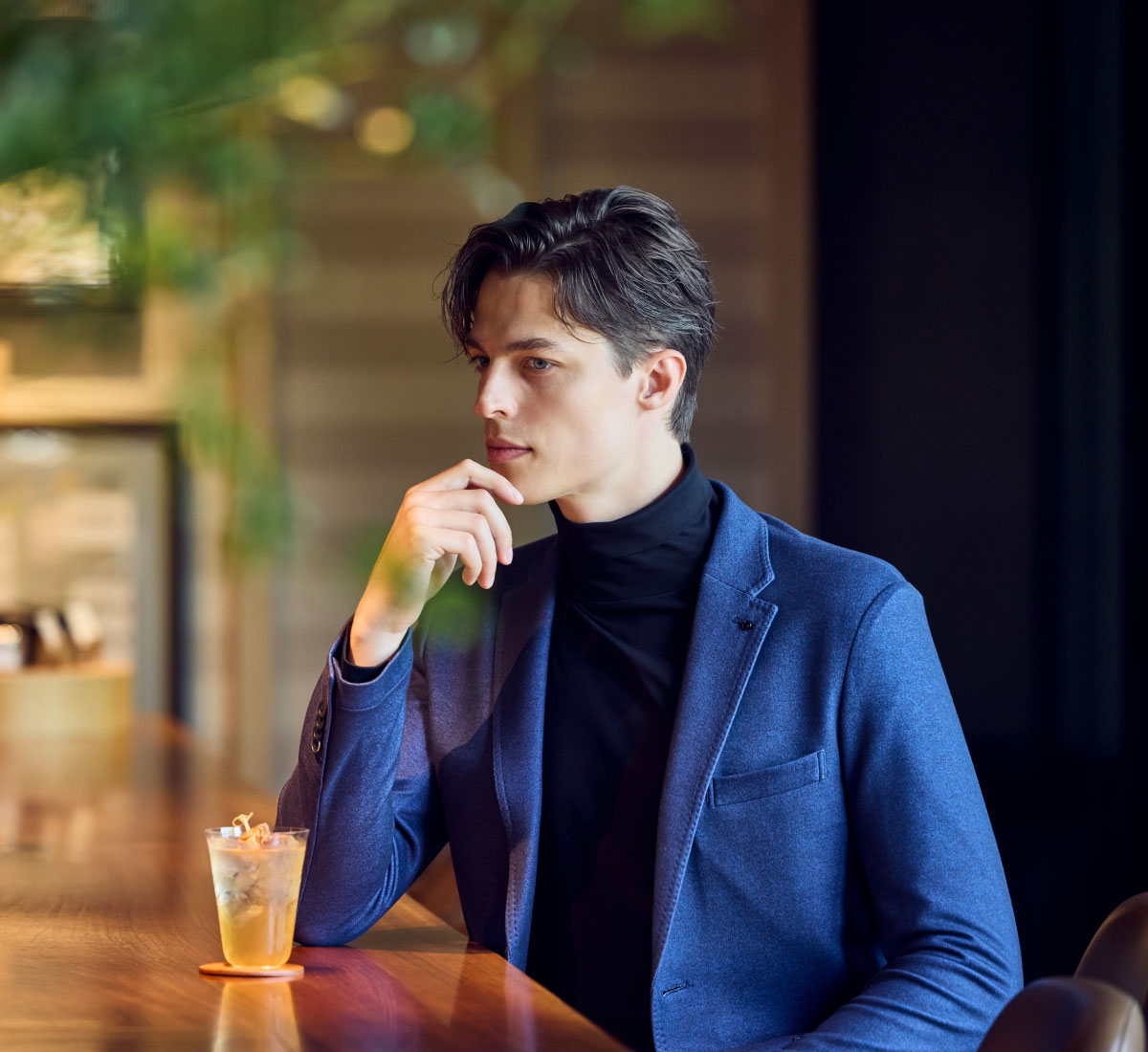 ネイビーのジャケットセットアップ・ブラックのニットを着用した,ホテルに設置されている大人っぽい雰囲気のあるバーカウンターに座っている男性