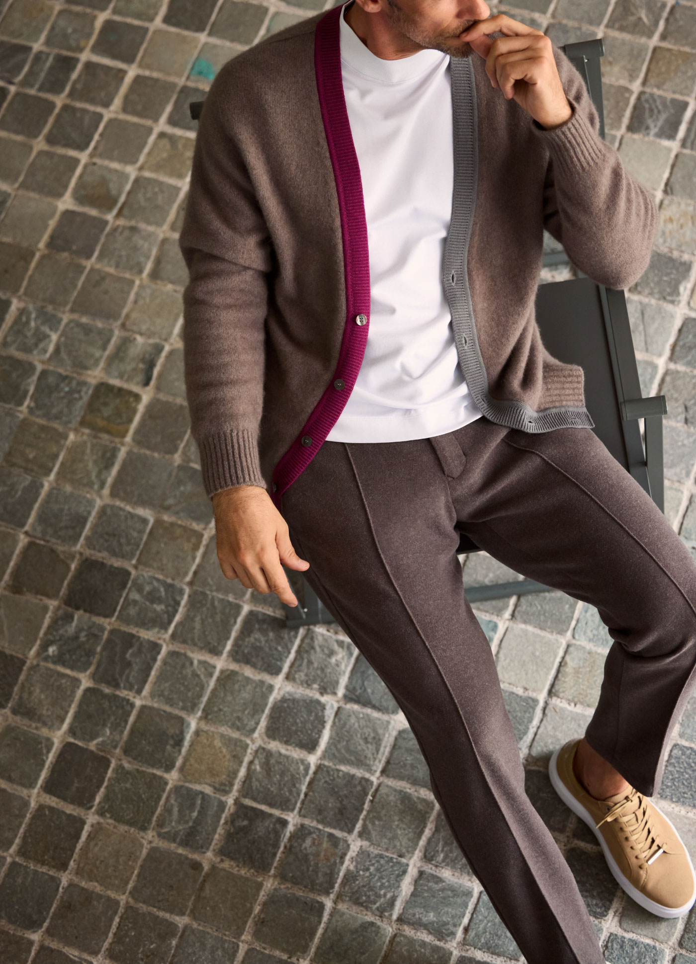 ブラウンのカーディガン・ホワイトのトップス・ブラウンのパンツを着用した男性が椅子に座って遠くを眺めている様子