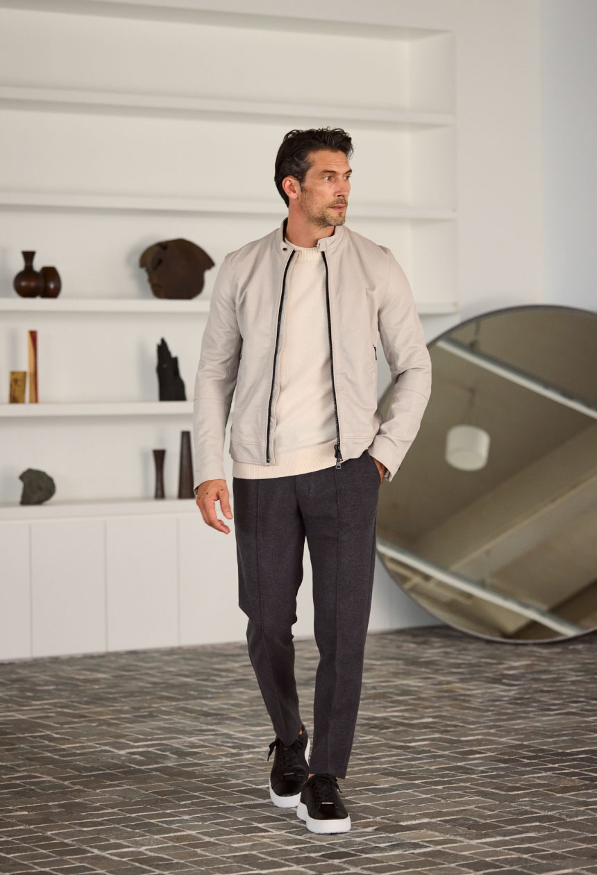 アイボリーのライダースジャケット・オフホワイトのトップス・チャコールグレーのパンツ・ブラックのスニーカーを着用した男性