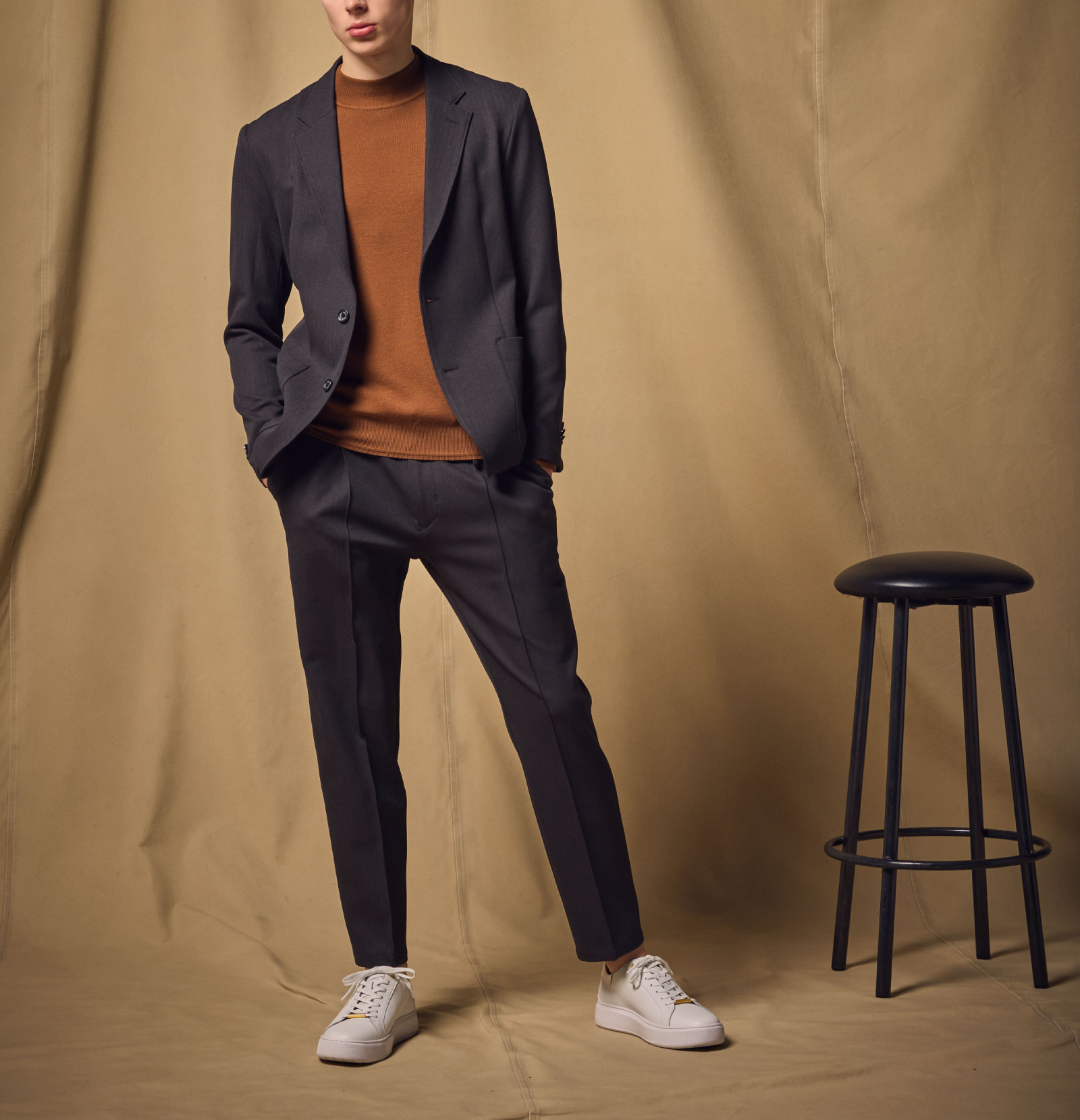 ブラックのジャケットのセットアップ・ブラウンのニット・ホワイトのスニーカーを着用した男性