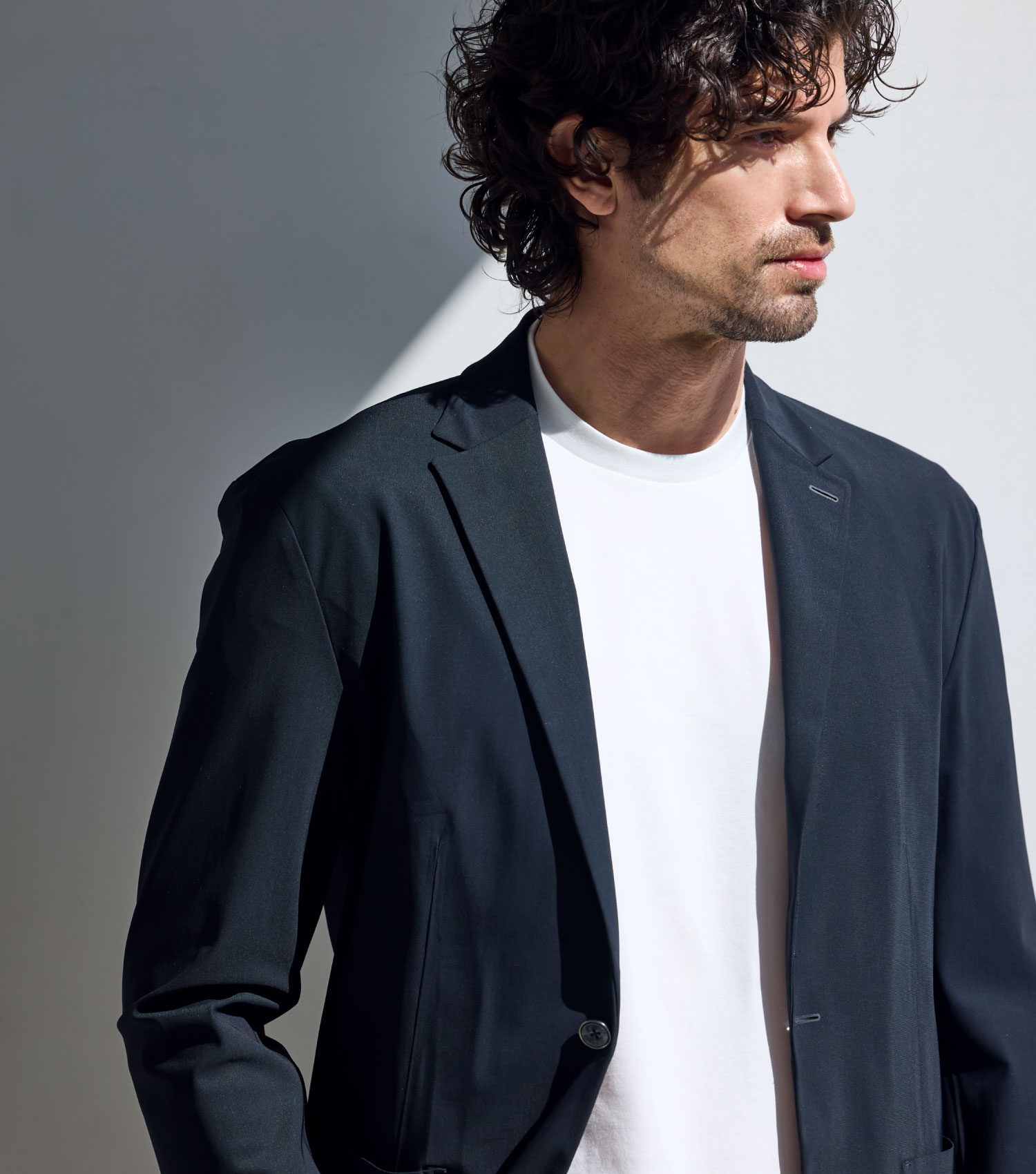 ホワイトのPACK T-SHIRTとジャケットを着用したパーマのかかった外国の男性が右方向を向いている様子