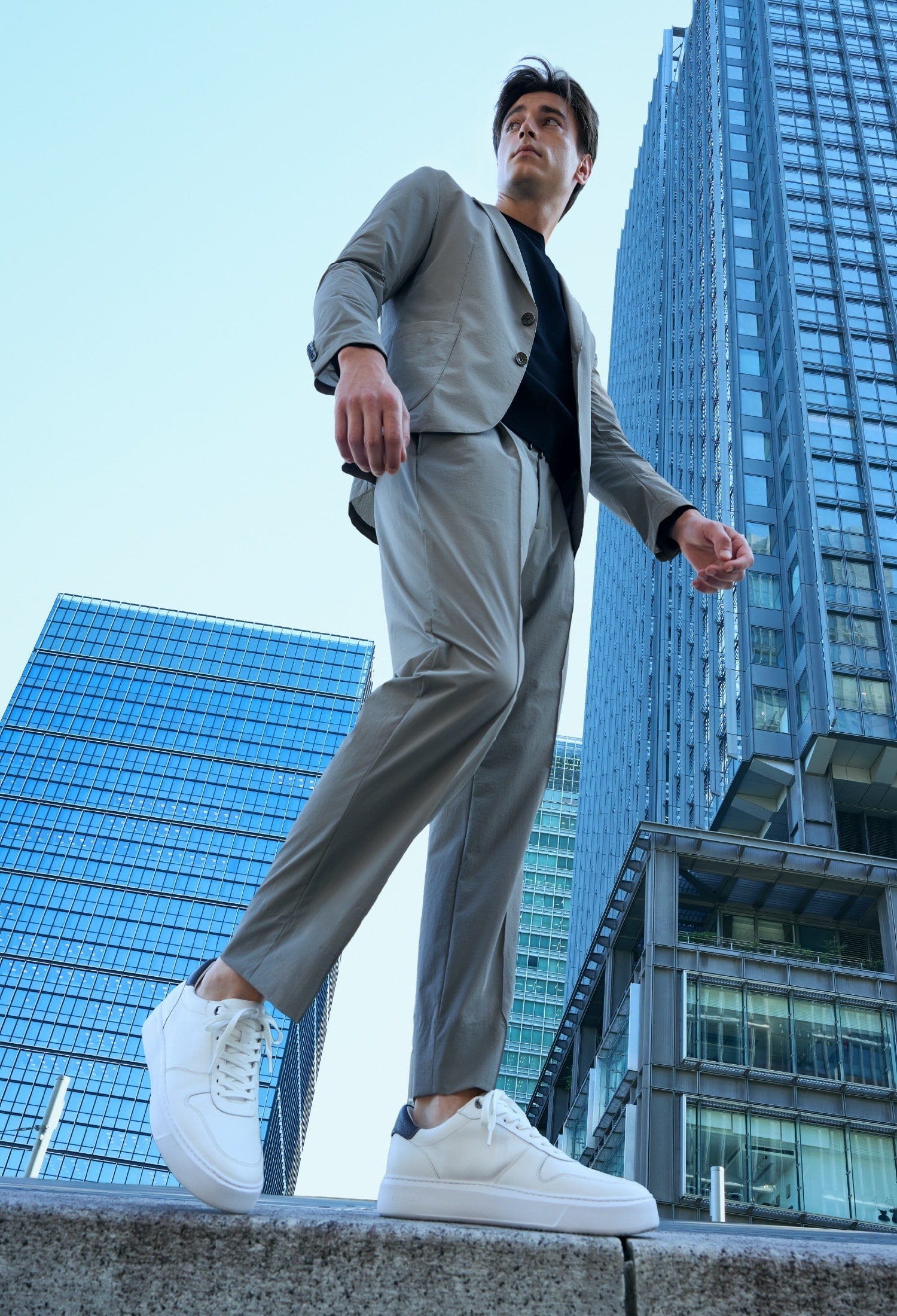 白のスニーカーとライトベージュのスーツのセットアップ、黒のニットのコーディネート