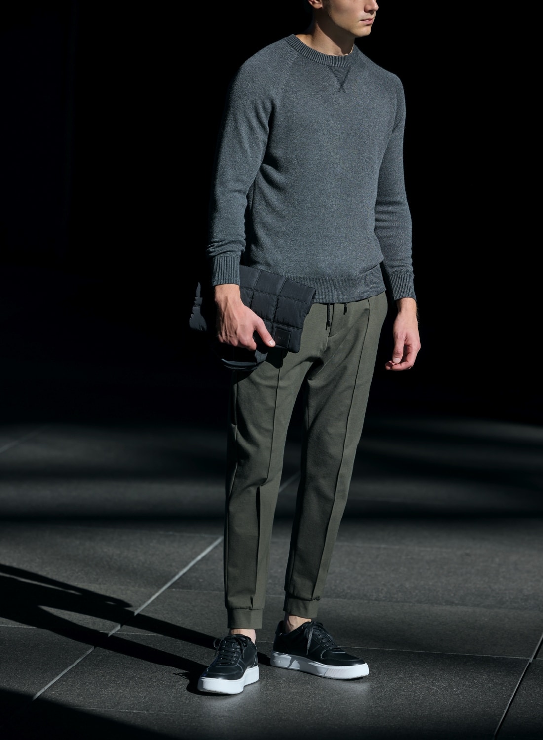 白のスニーカー、チャコールグレーのプルオーバーにカーキのリブパンツのラフなコーディネート