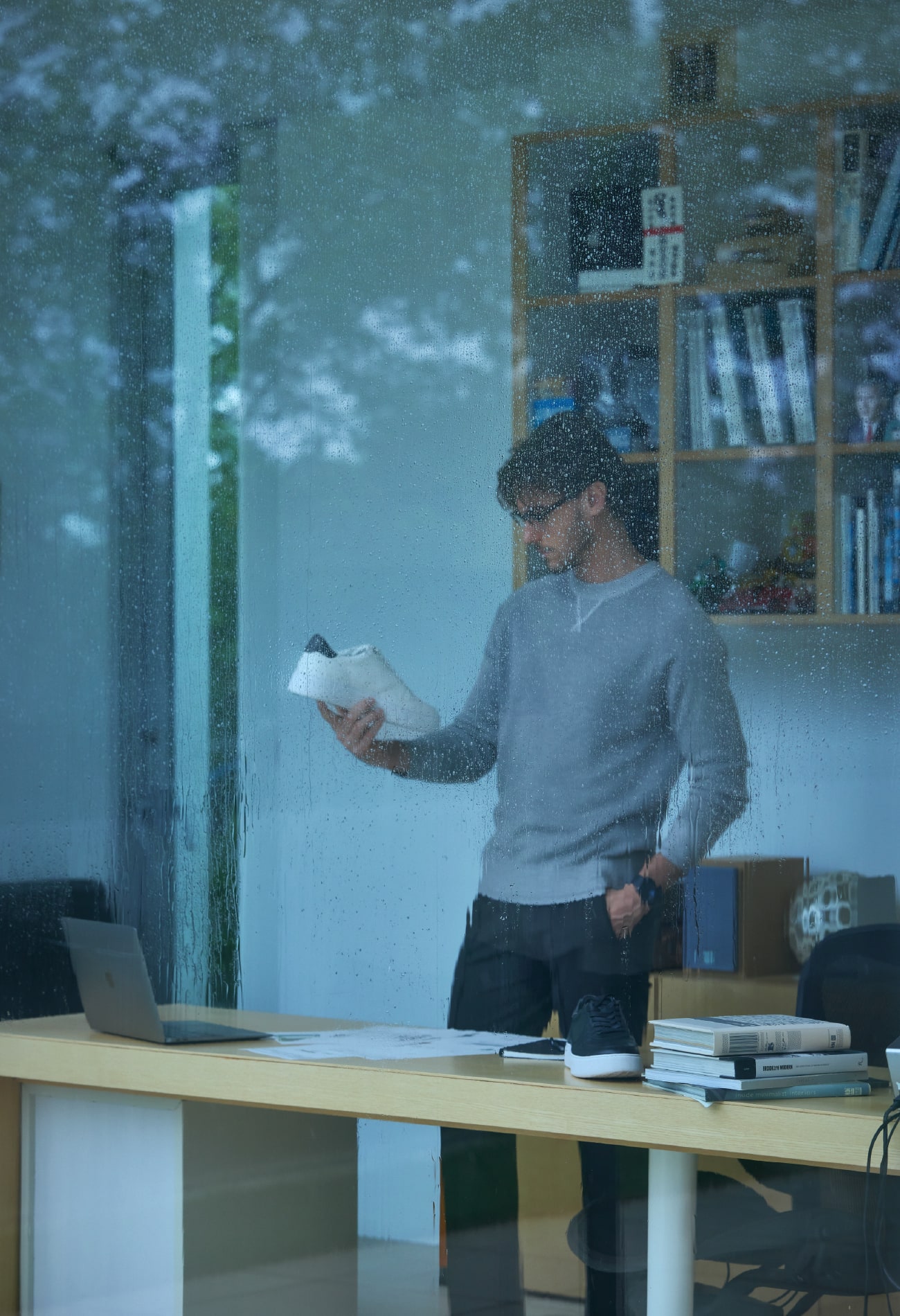 雨が降る屋外からガラス越しに男性を写した画像。PCを開き仕事に没頭する男性が着ているのは、スウェットライクニット プルオーバーとハイブリットトロピカル パンツ。