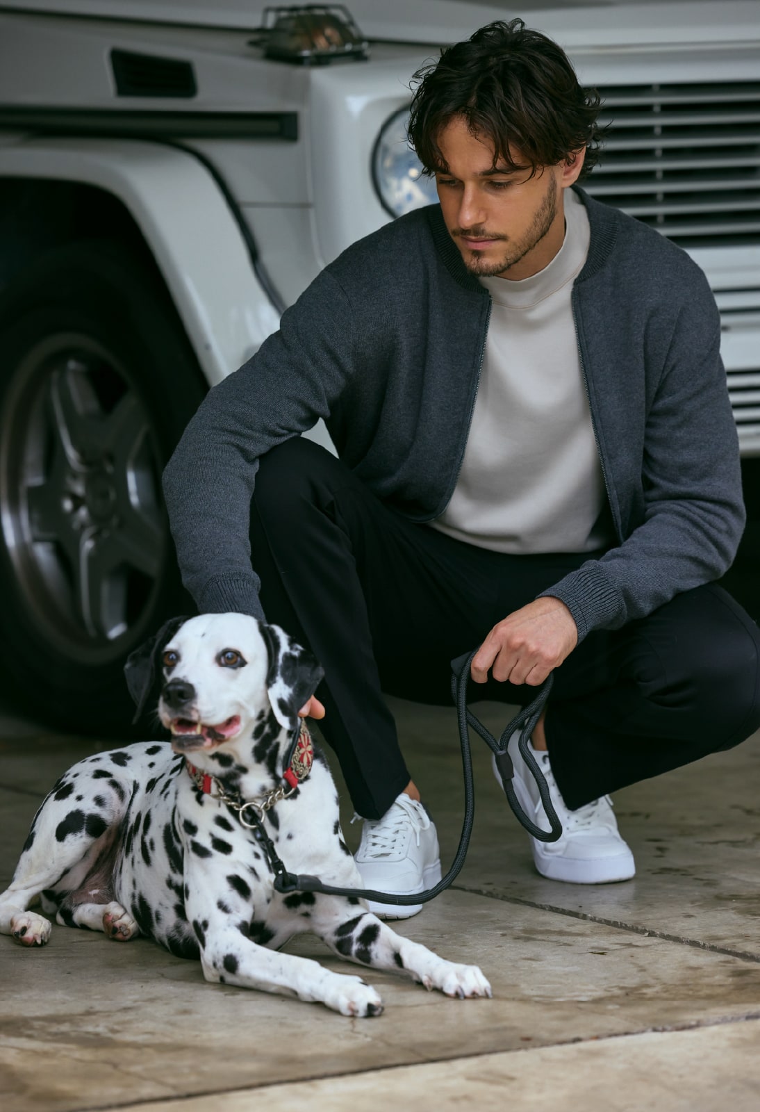 ブルゾン・カットソー・パンツのコーディネートで犬と一緒にしゃがんでいる画像。