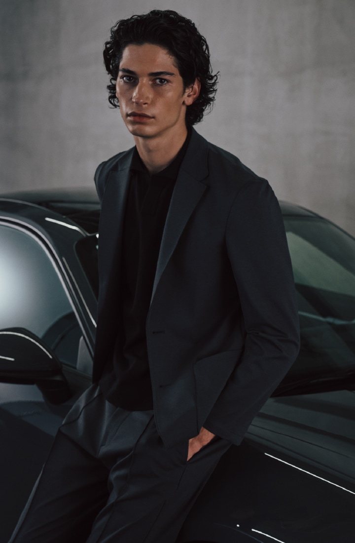 グレイのジャージーセットアップとブラックのポロシャツを着た男性のビジュアル