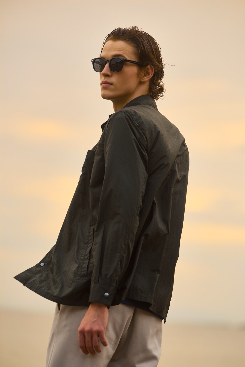 浜辺でのブラックアウターとライトグレーパンツの着用カット
